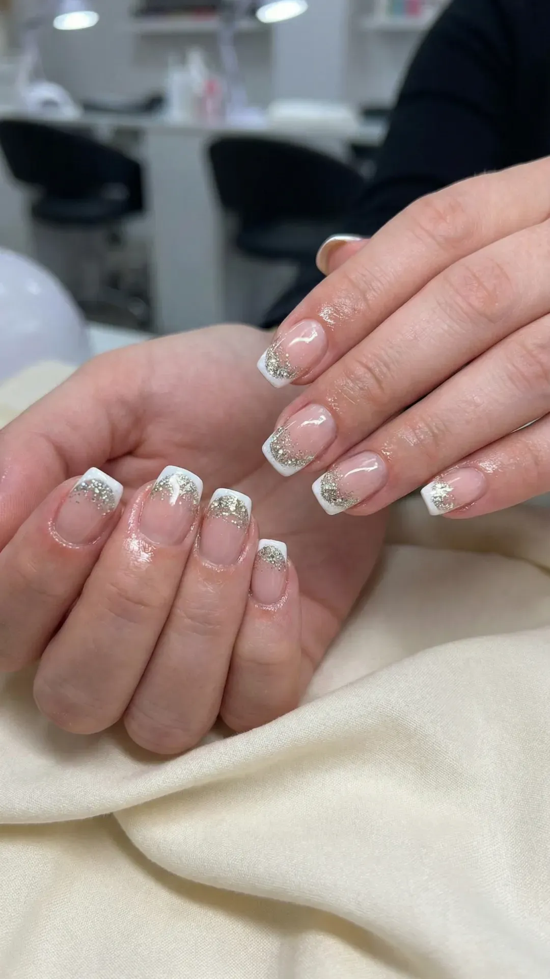 Short square French tip nails with silver glitter fade tips, salon setting background
