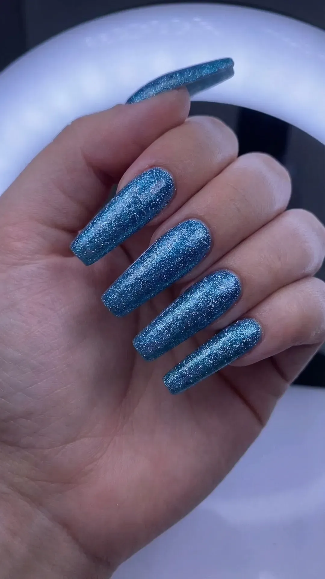 Long coffin nails painted metallic blue glitter polish, cool LED lighting glow
