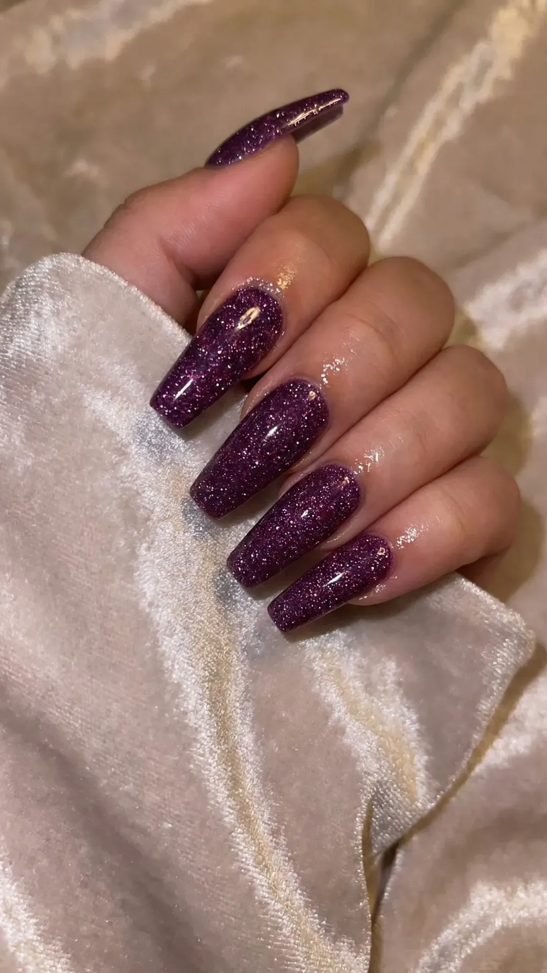 Long coffin nails with deep purple glitter polish, glossy finish on satin background
