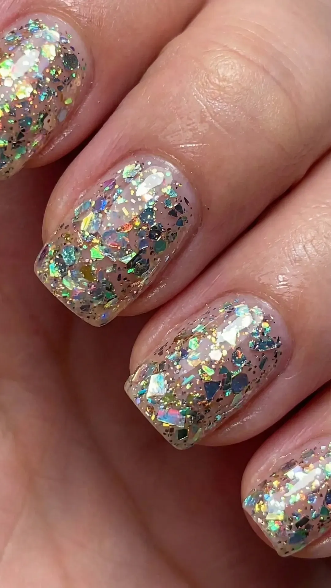 Close-up of short square nails with chunky holographic glitter pieces over nude base