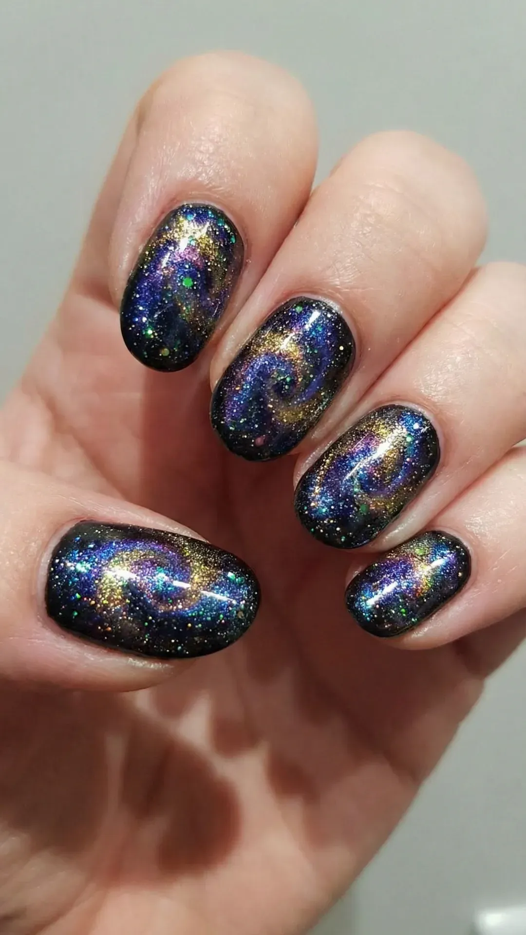 Short rounded nails with galaxy nail art featuring stars, nebula colors, and holographic glitter