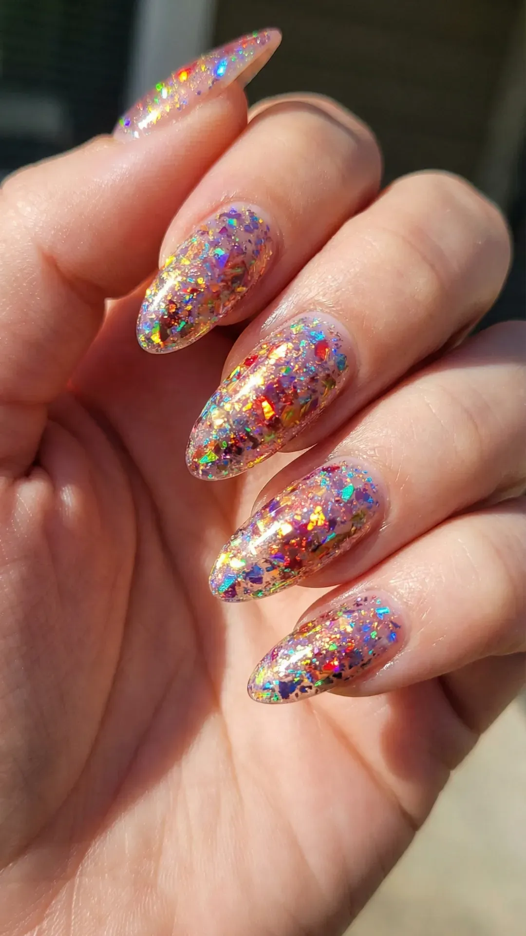 Almond nails with holographic multicolor glitter flakes reflecting rainbow light in sunlight
