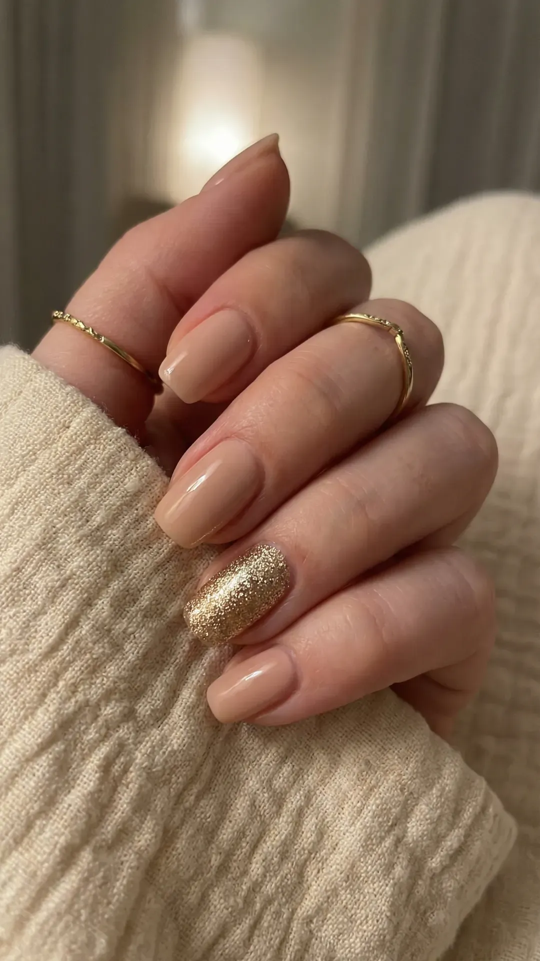 Nude glossy nails with one gold glitter accent nail, cozy sweater background