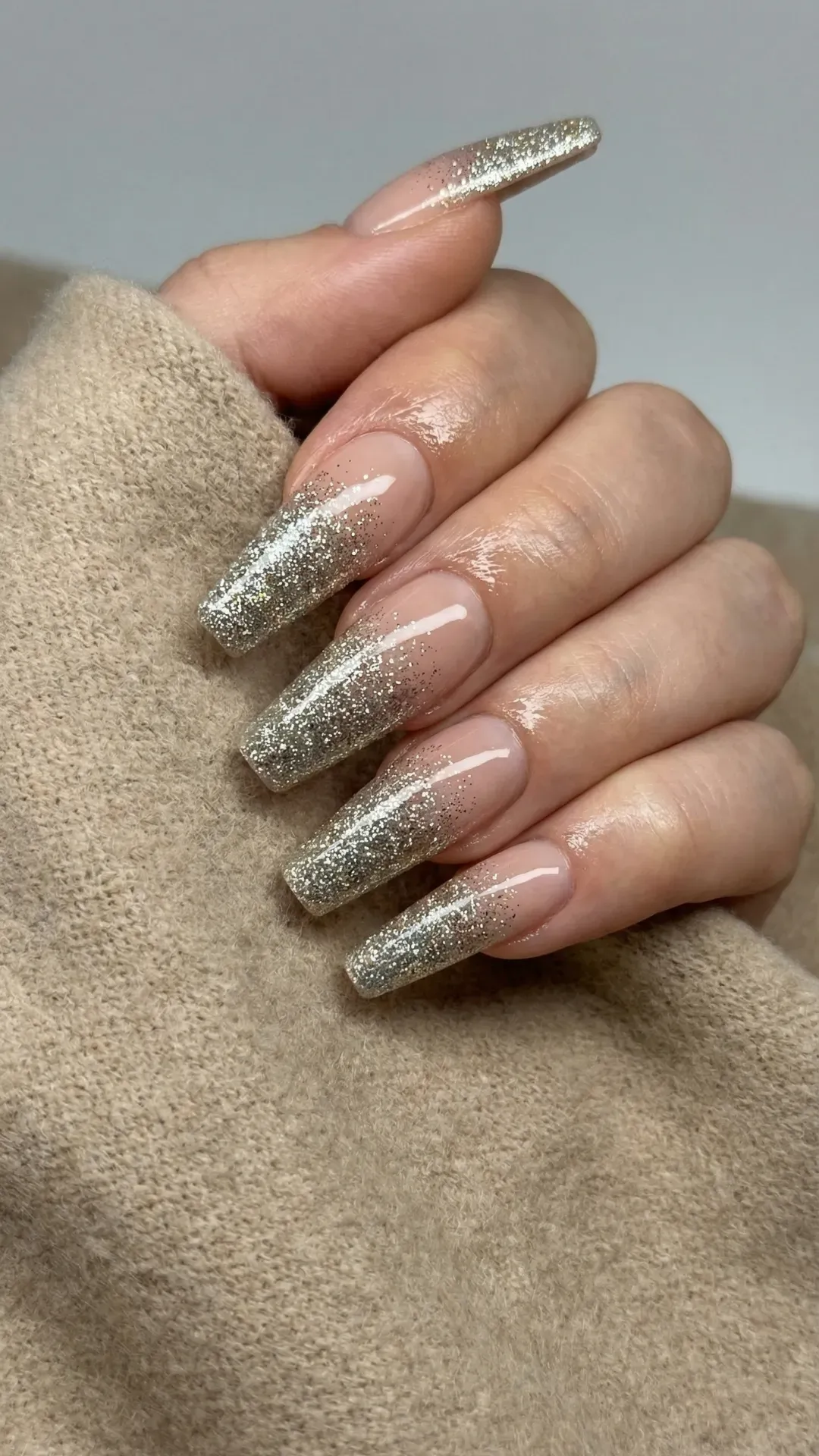 Long coffin nails with silver glitter ombre fade over nude base, glossy finish