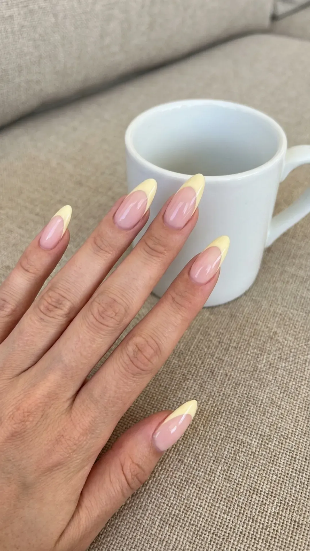 Soft yellow-tipped almond French nails providing a delicate and subtle pop of color for a sunny manicure.