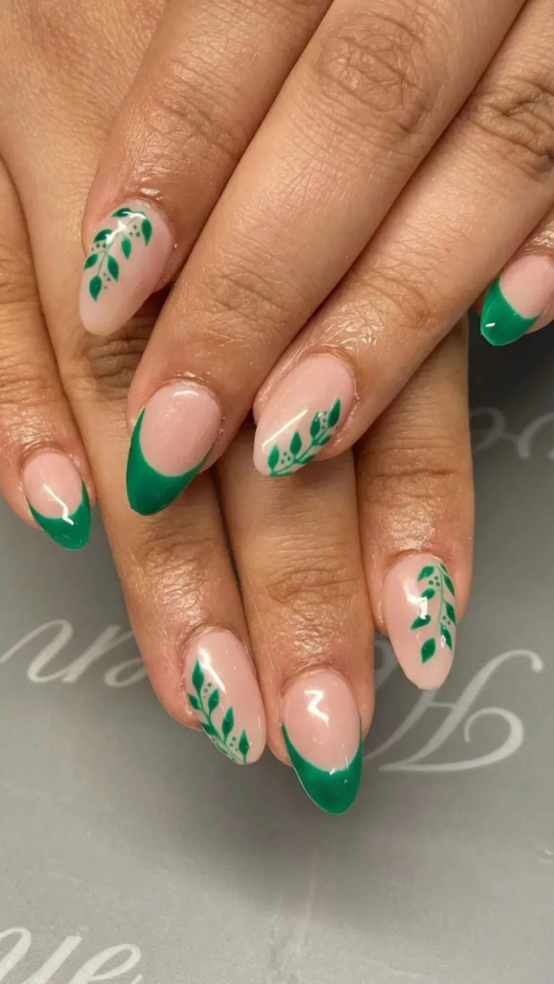 Nature-inspired muted green French tips with leaf designs on almond nails for an organic and chic look.
