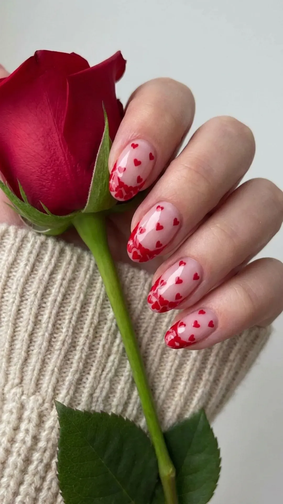 Short nails featuring a playful twist on French tips with red hearts scattered on a translucent pink base, perfect for a Valentine's Day look.