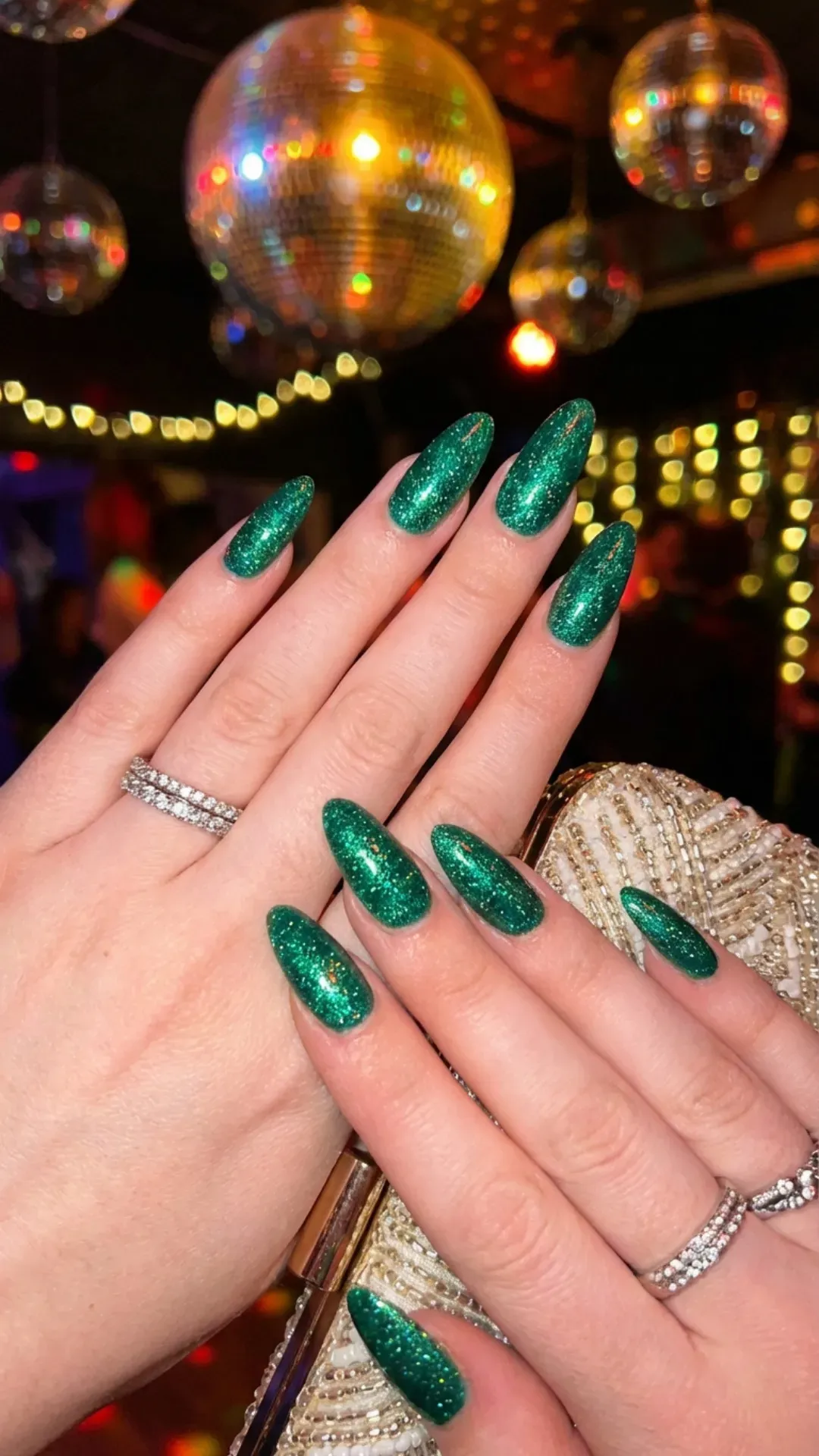 Sparkling emerald green almond nails with fine glitter under disco lights