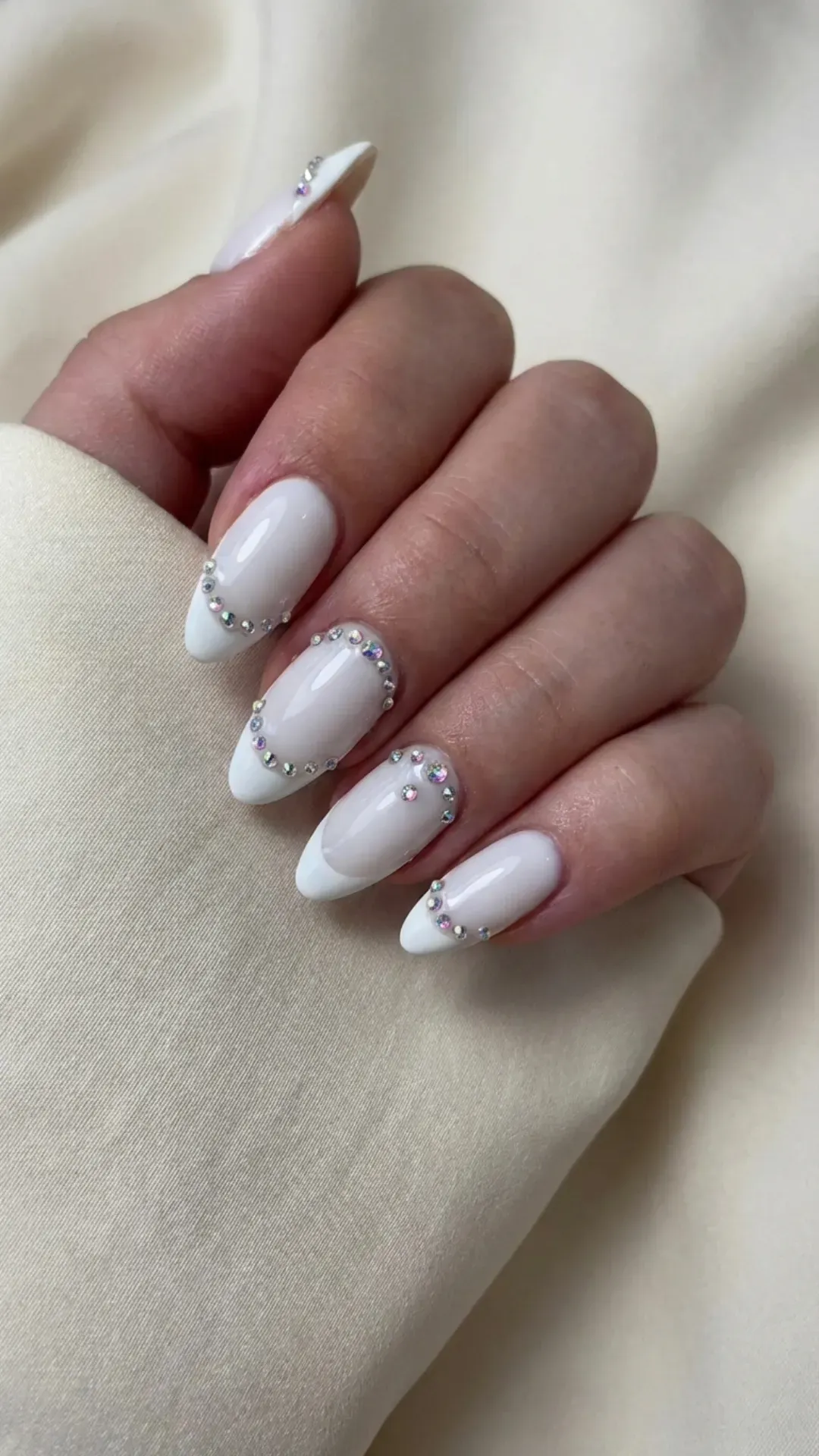 Glamorous almond French tip nails adorned with rhinestones on a white base, perfect for a luxurious and sparkling look.