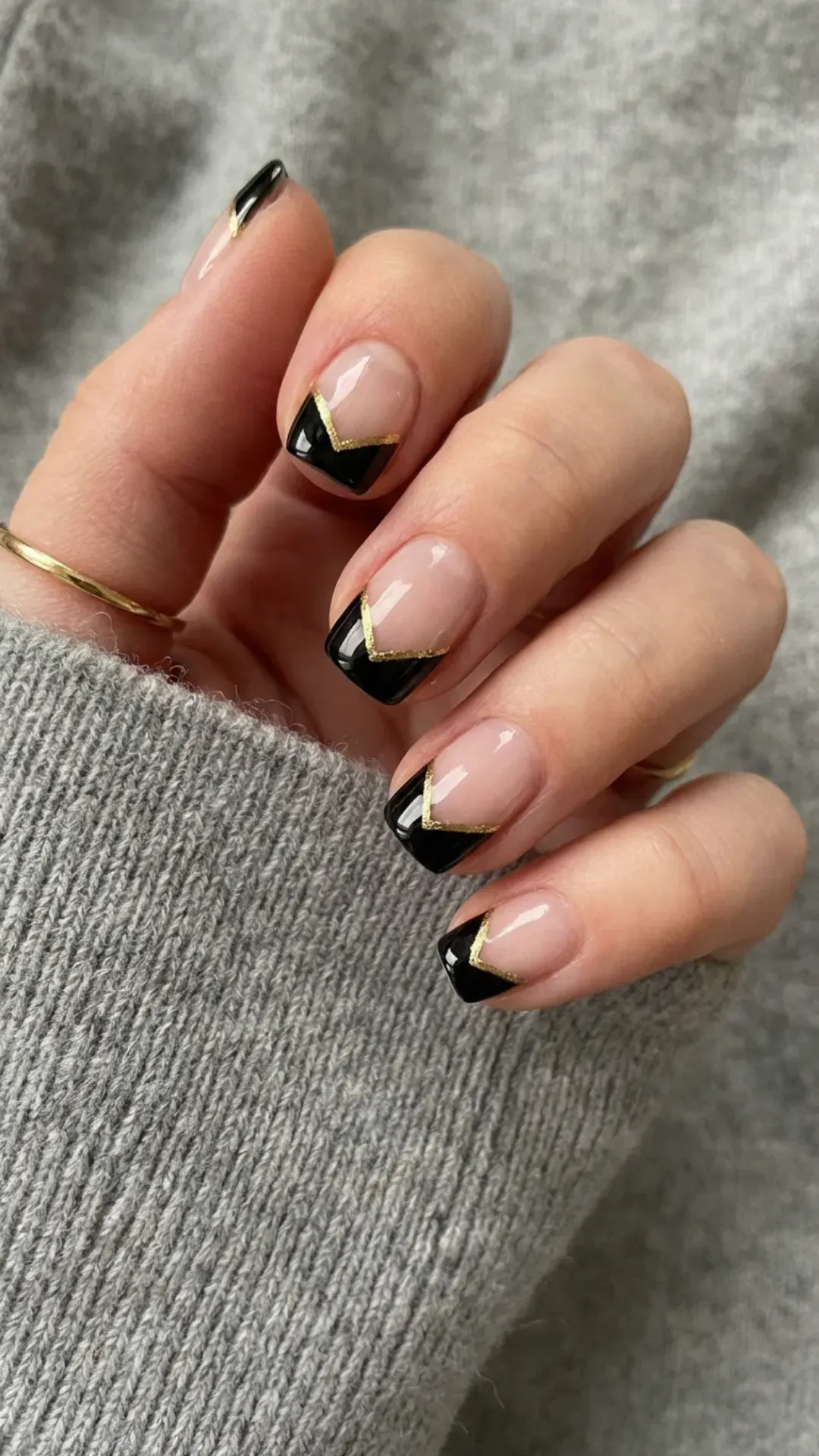 Short french tip nail with a bold chevron French tip design in black and accented with a thin gold stripe, providing a chic and modern nail art style.