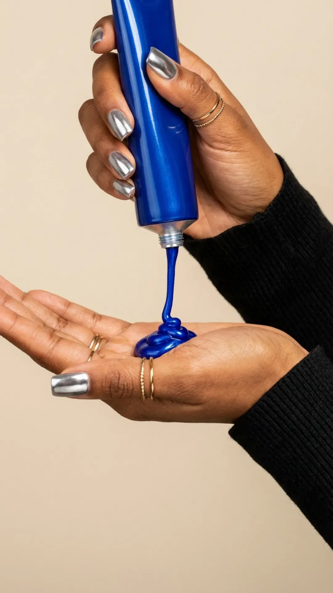 Close up of hands with bronze skin and silver chrome square nails dispensing blue toning hair mask.