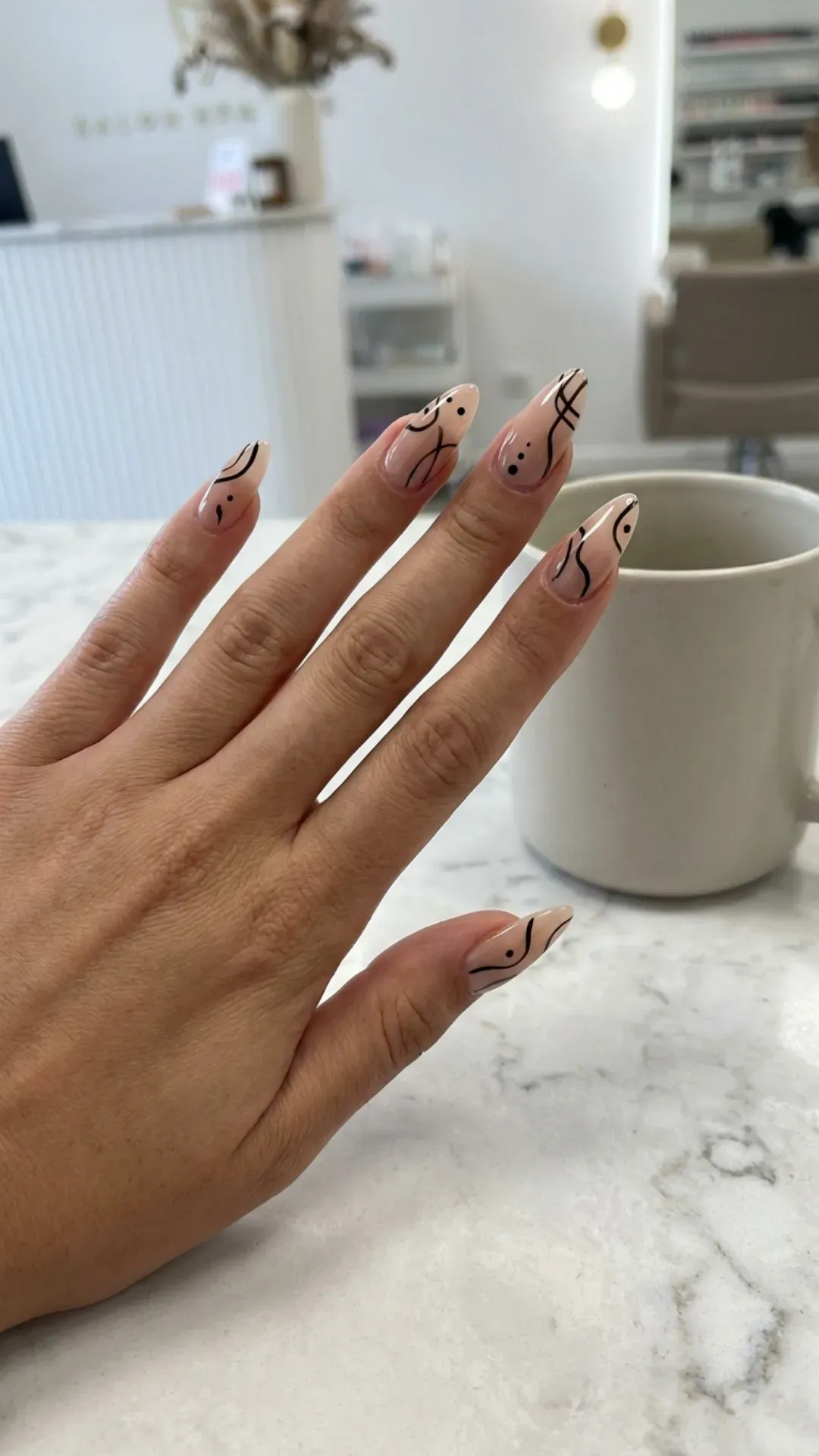 Nude stiletto nails with minimalist abstract black line art