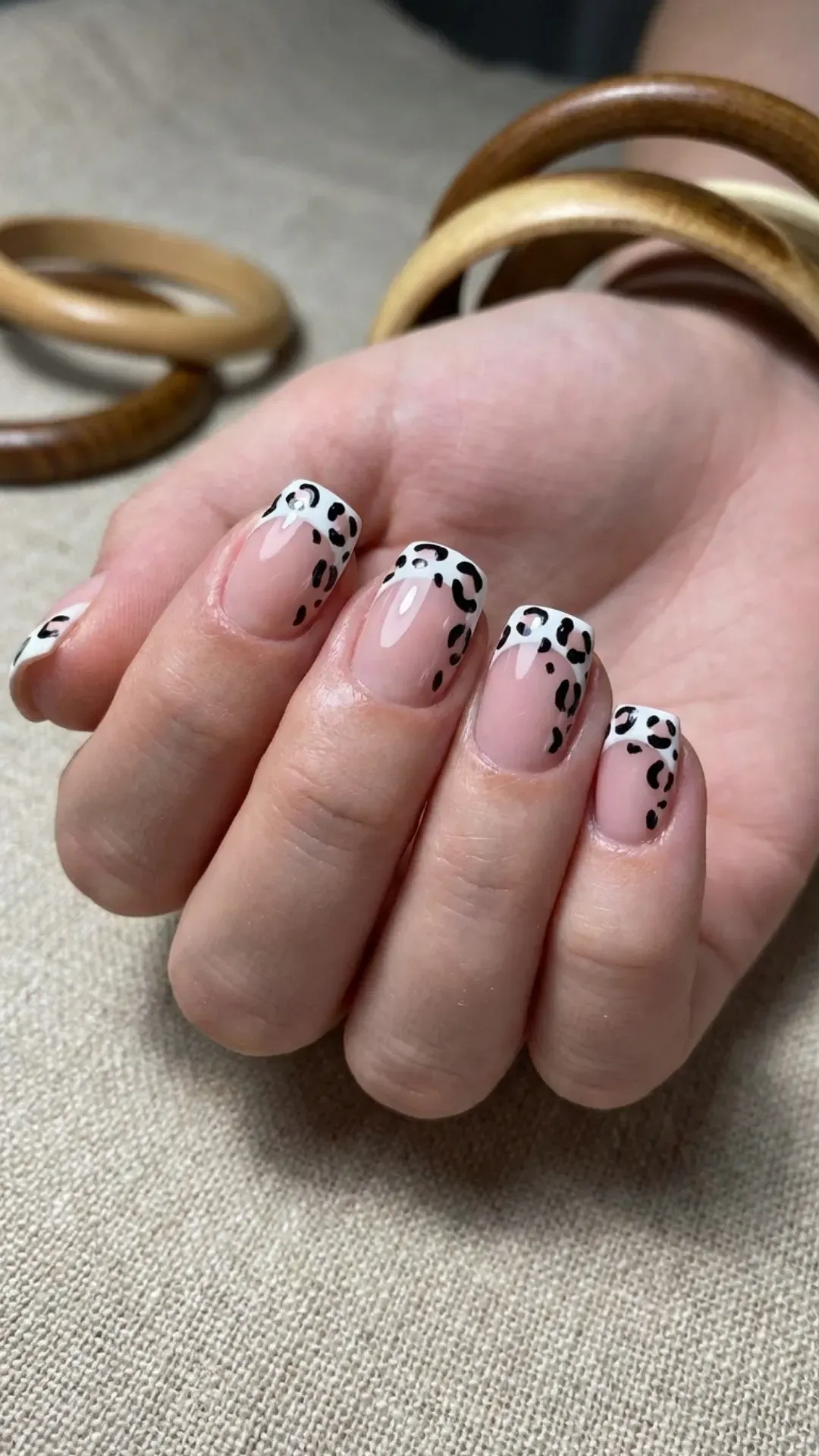 Bold and playful short nails with an animal print design on French tips, pairing a natural base with black spots for a wild touch.