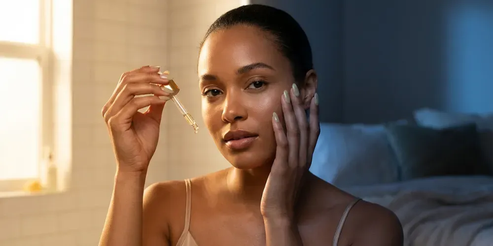 Woman with glowing skin demonstrating morning and night skincare routines with split lighting, wearing a silk camisole and sheer matcha nails.