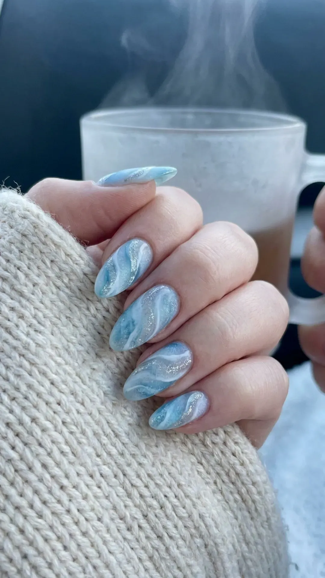 Chilly icy blue nails with silver glitter accents embodying a frosted marble look, perfect for a winter-inspired manicure.