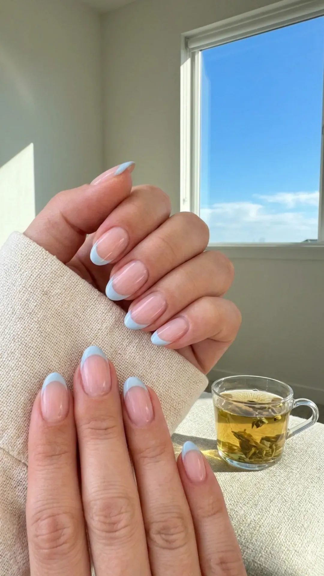Calm and collected nails with a sheer pink base and serene light blue French tips, reminiscent of a clear sky.