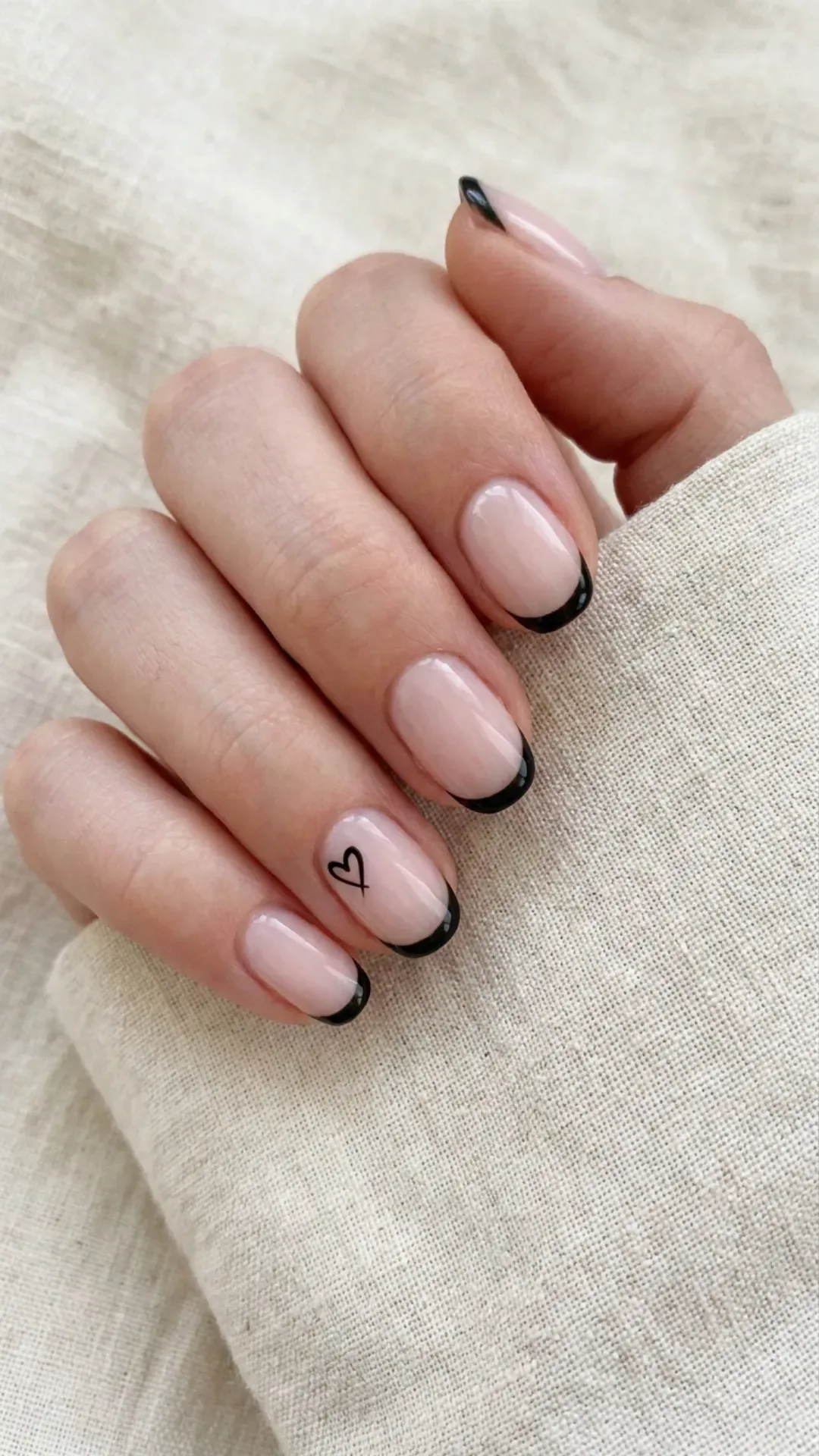 Unique and minimalist French manicure with a sheer base, outlined tips, and a single black heart for a touch of romance.