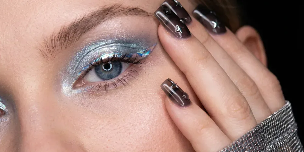 Close-up of holographic silver and blue eyeshadow with graphic metallic liner and 3D cyber nail art with gel droplets.