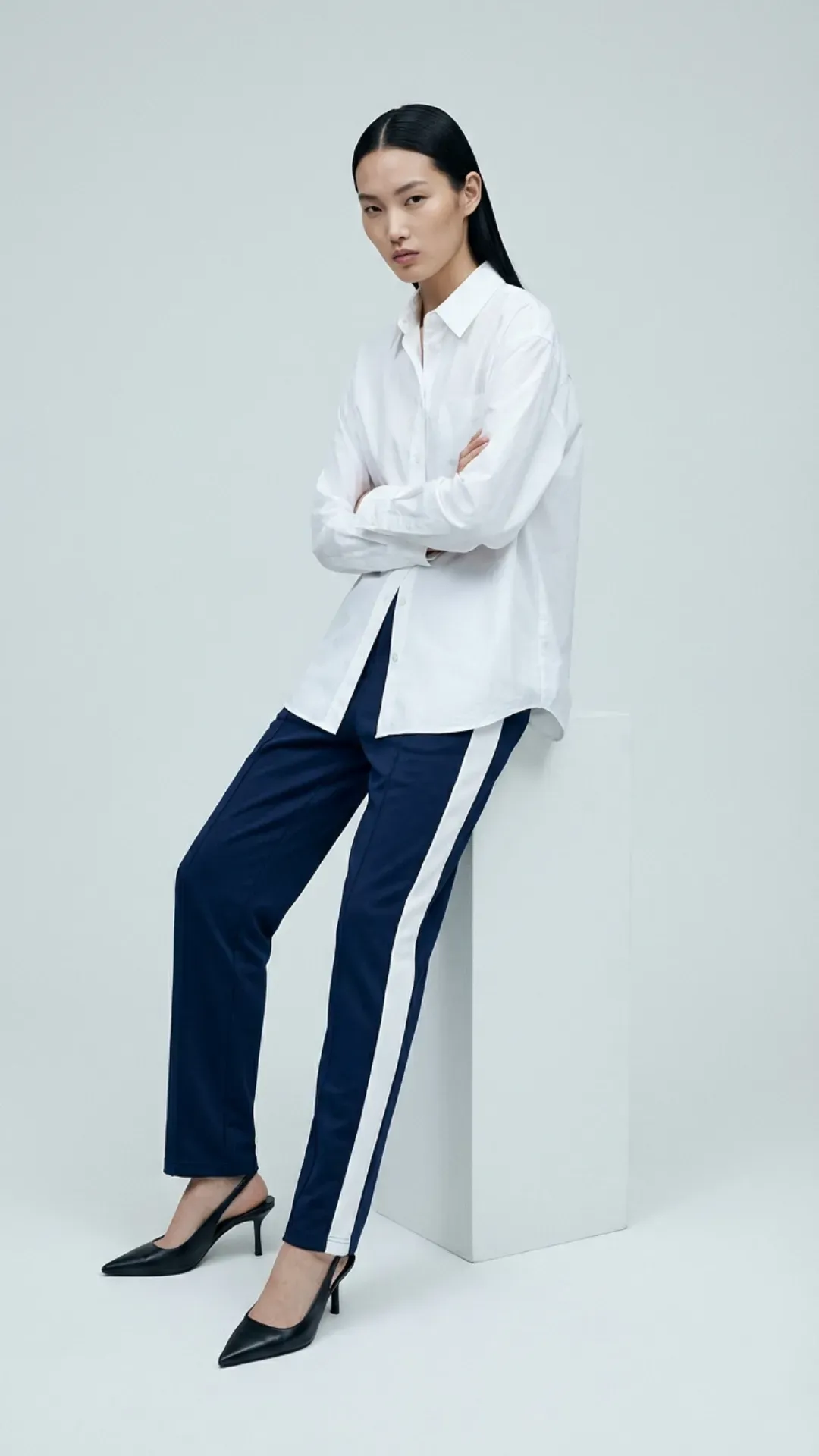 Navy track pants styled with a button-down shirt and heels for a trendy sportif look.