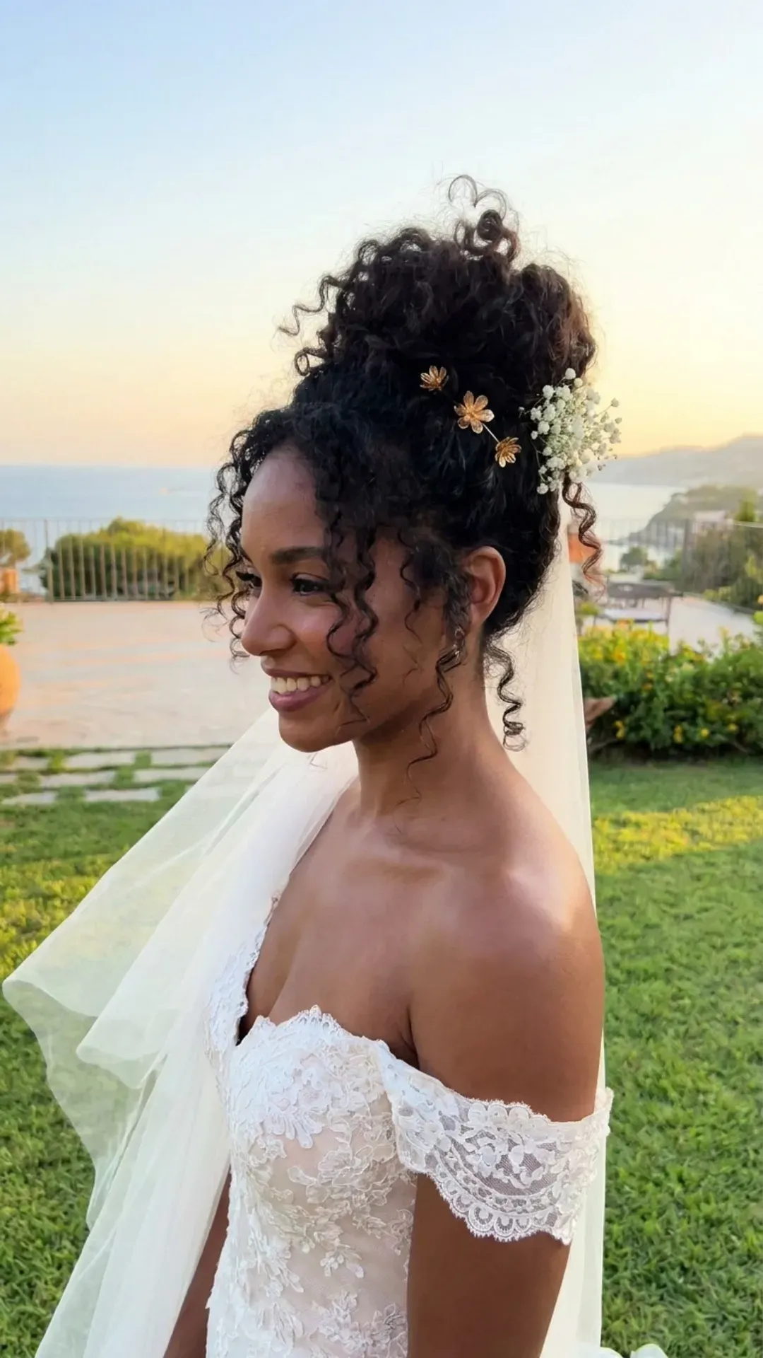 Elegant wedding hairstyle featuring a top knot with voluminous natural curls, perfect for a summer bride seeking a sophisticated yet breezy look.