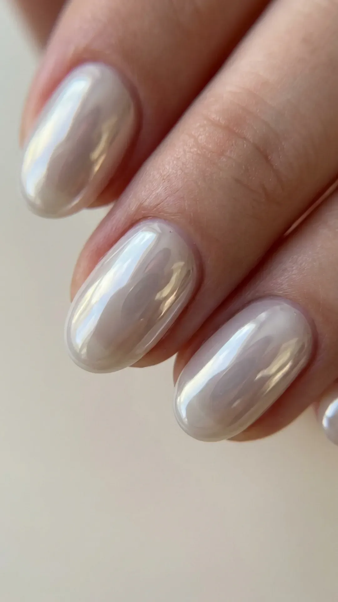 Short oval nails with ultra-glossy glass skin chrome finish in translucent pearl white, reflecting natural sunlight — summer 2026 nail trend
