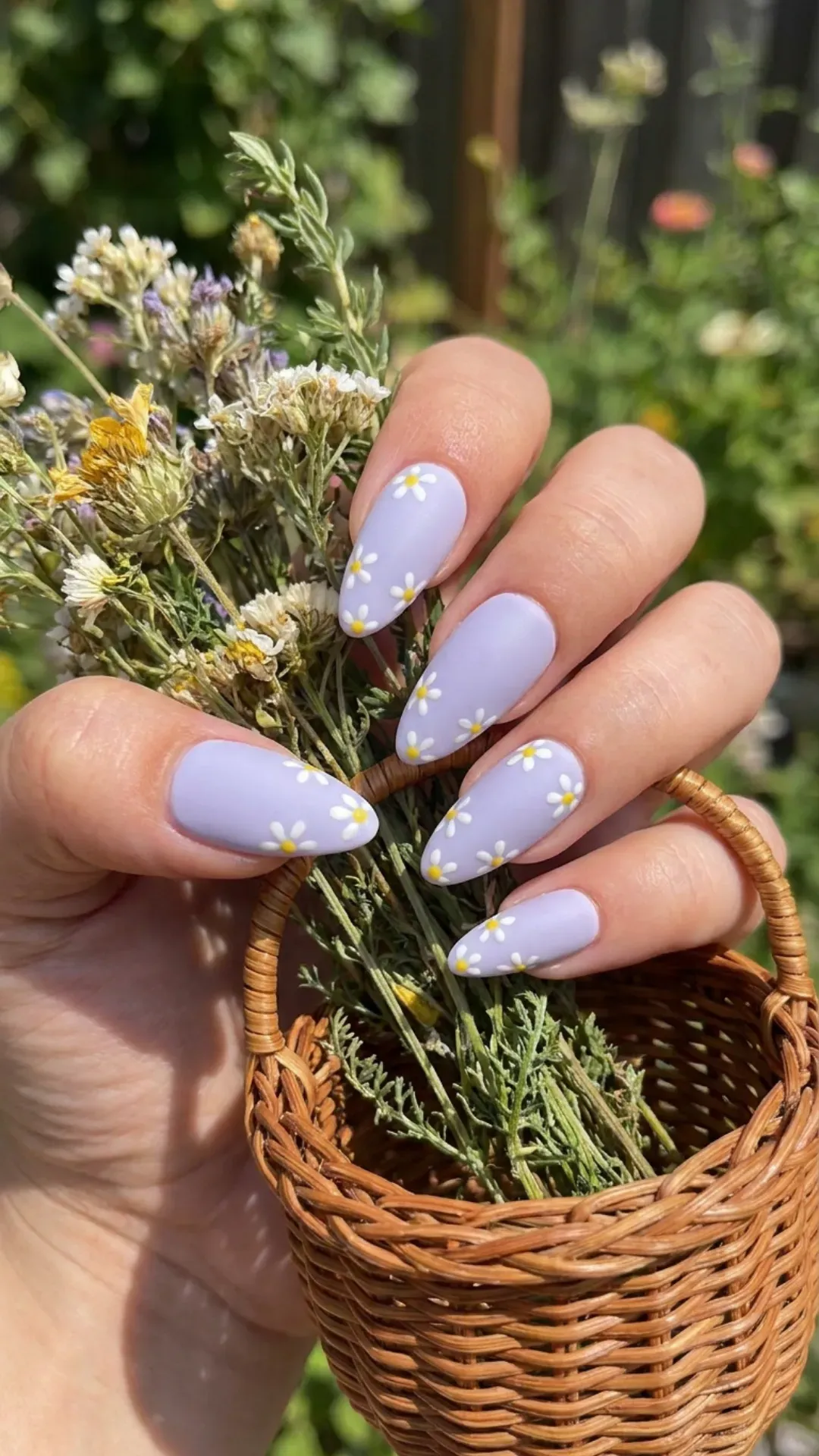Almond-shaped nails painted in a soft lavender shade featuring delicate white daisies with yellow centers on each nail, embodying a spring-inspired, floral nail art design.