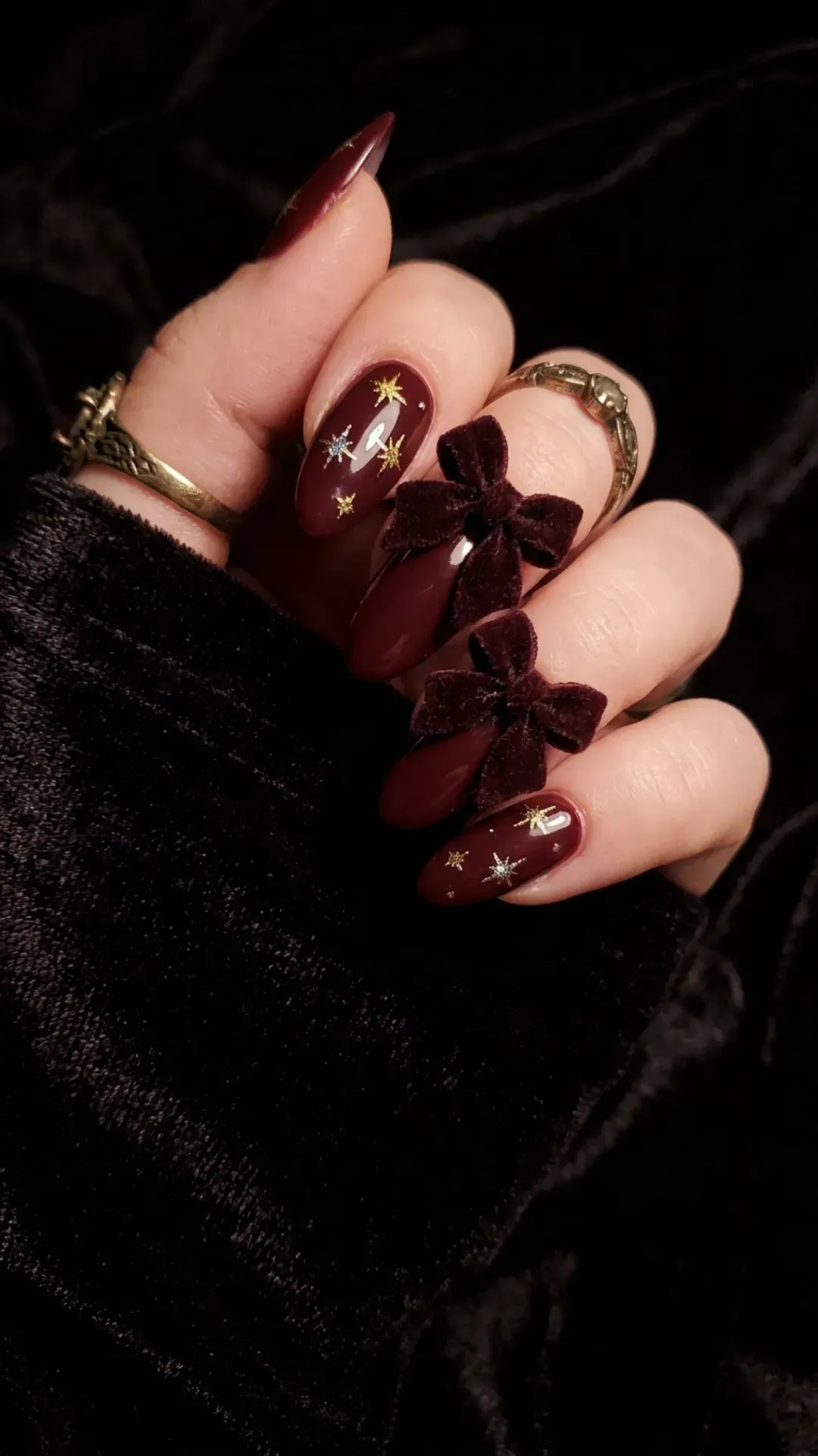 Maroon nails featuring large bows and delicate starburst designs, creating an elegant and mysterious look.