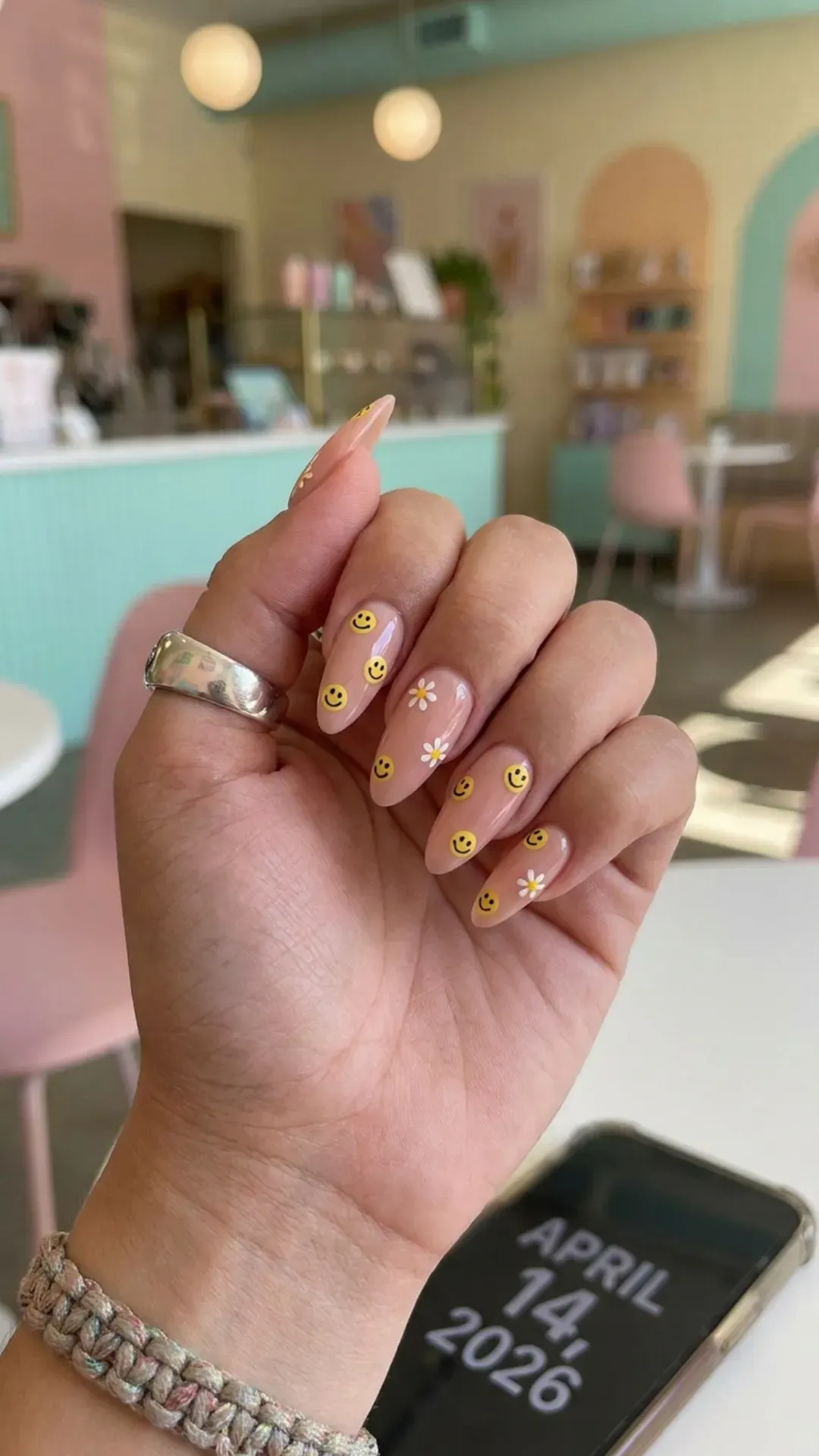 Long acrylic nails with a nude pink base adorned with cheerful yellow smiley face decals, perfect for a playful yet chic look in 2026. 