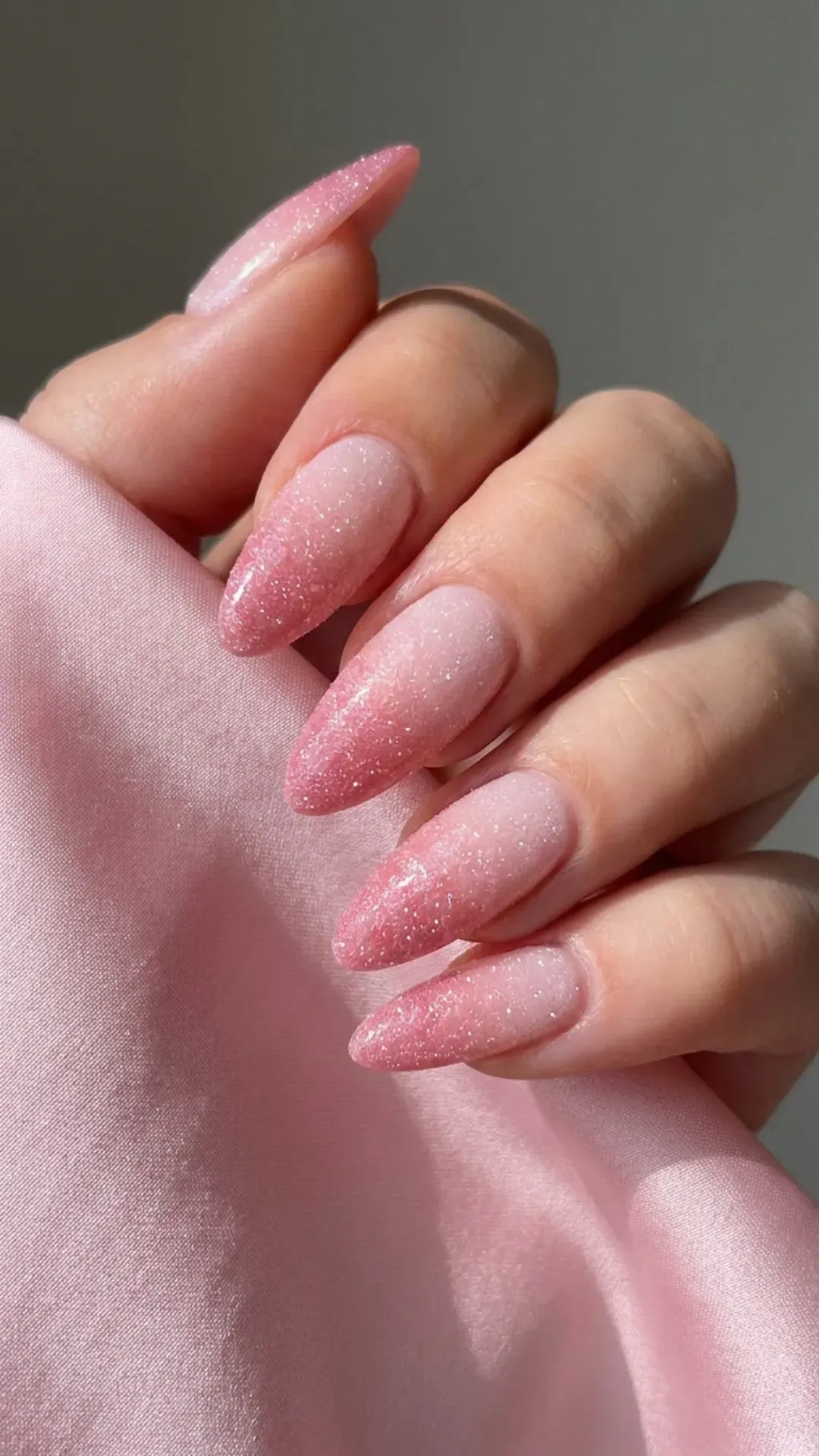 Long nails with a gradient of pale to deeper pink, topped with a sugary shimmer reminiscent of a frosted petal