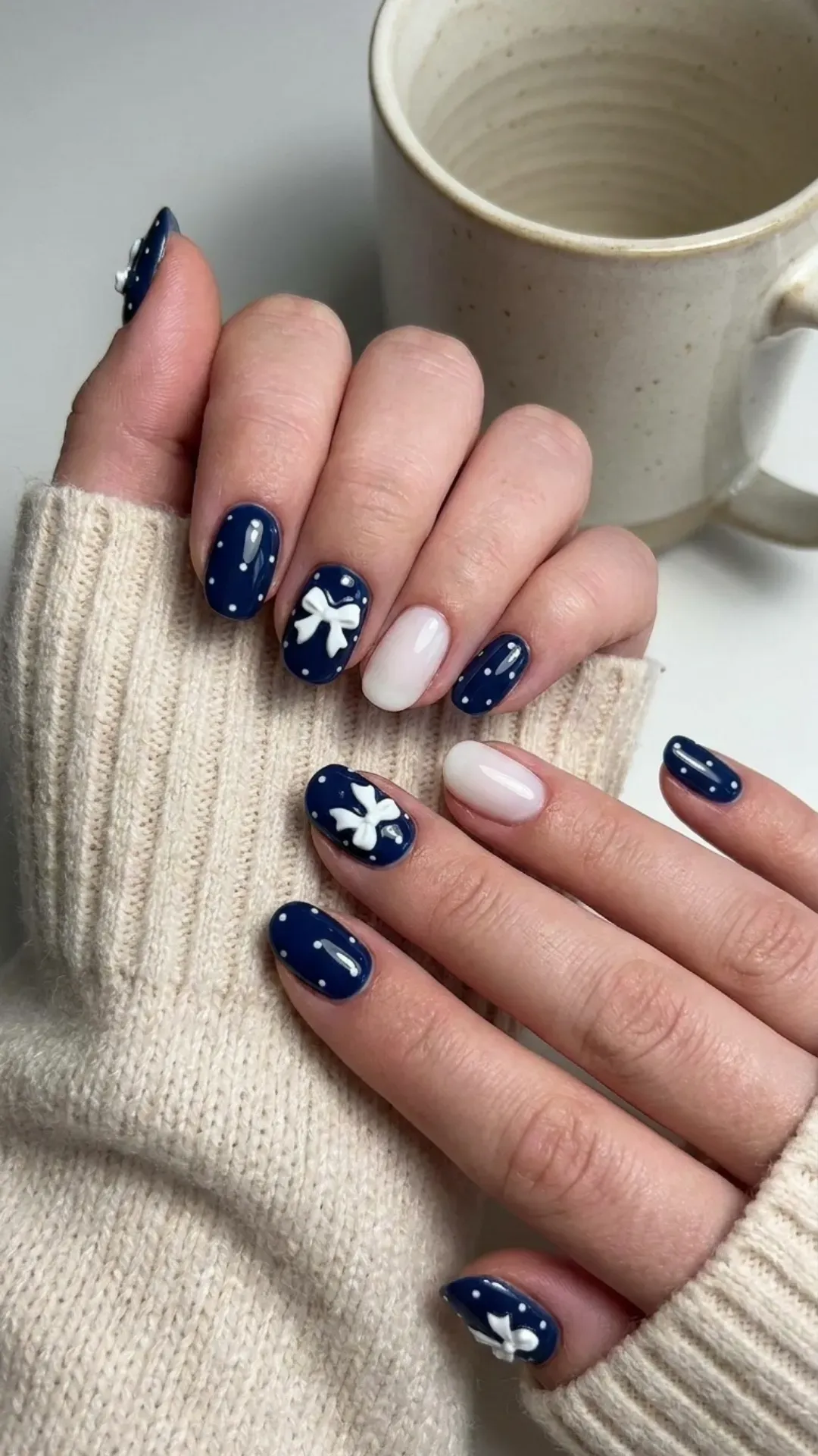 Deep navy blue nails adorned with coquette bows, dainty polka dots, and milky white accent nails for a classic yet playful style.