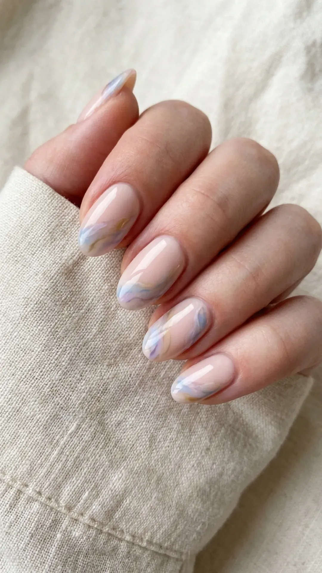 Nude pink nails featuring a subtle watercolor effect with wisps of translucent hues, offering an artistic and delicate nail art design.