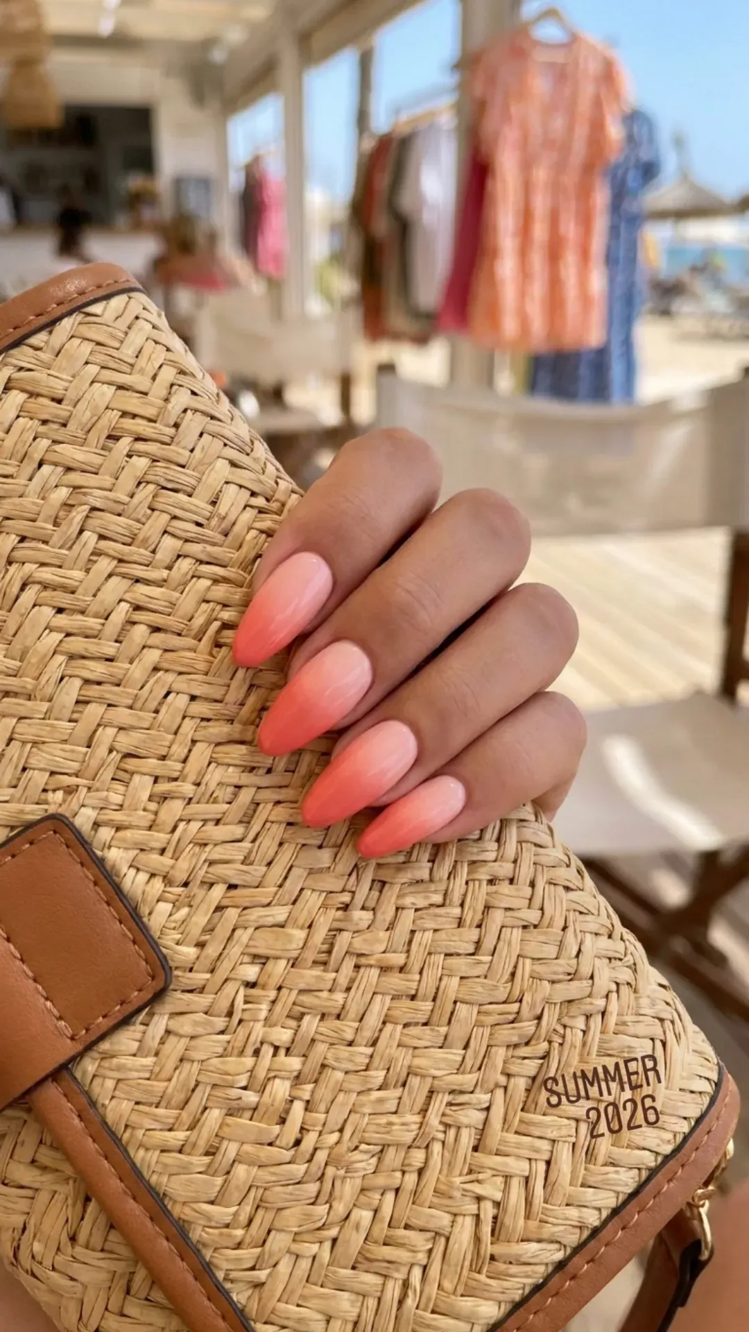 Gradient coral pink nails held against a purse, displaying a beautiful transition from light to dark pink shades for summer 2026.