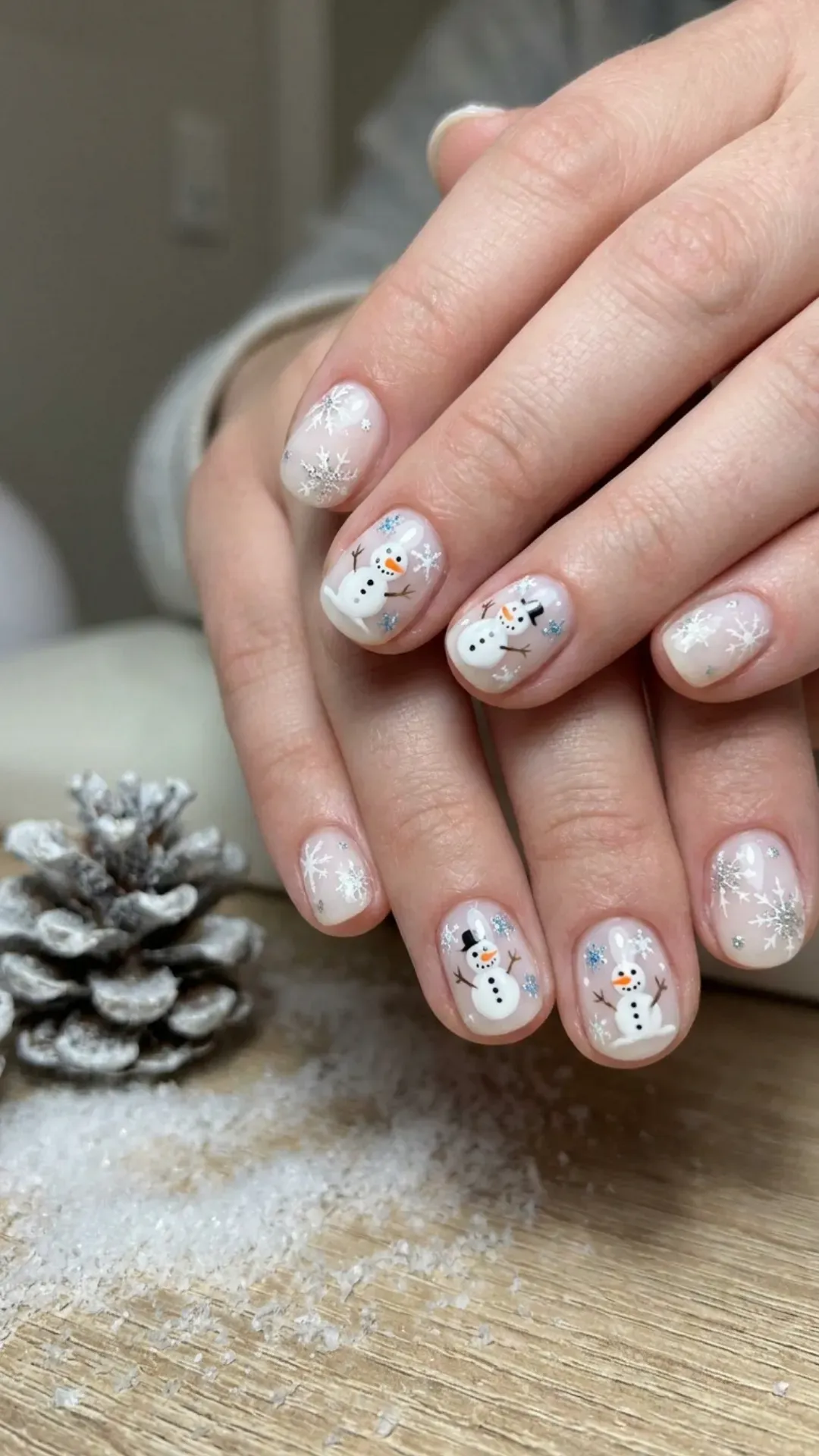 Cute short winter nails featuring playful snowmen and snowflake designs on a sheer white base, invoking a fun winter wonderland scene.