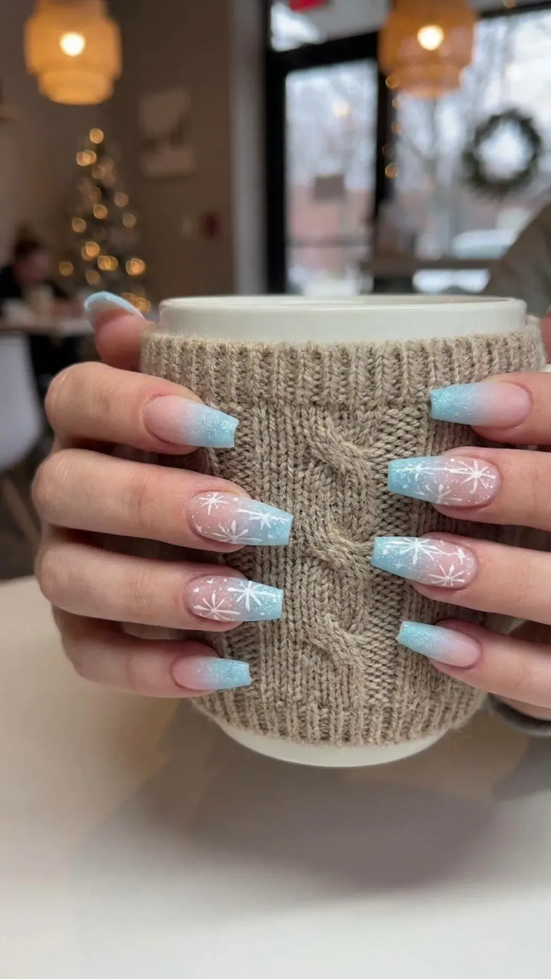 Trendy coffin-shaped nails with a winter wonderland vibe, featuring icy blue tips and delicate snowflake patterns for a chic look.