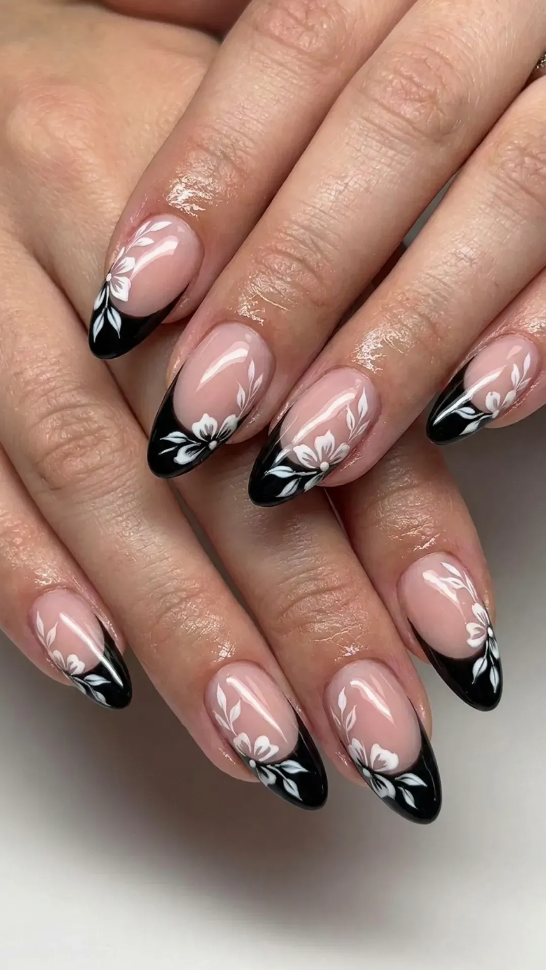 A modern take on the French manicure with glossy black tips and white floral designs, blending timeless elegance with a contemporary floral twist on each nail.
