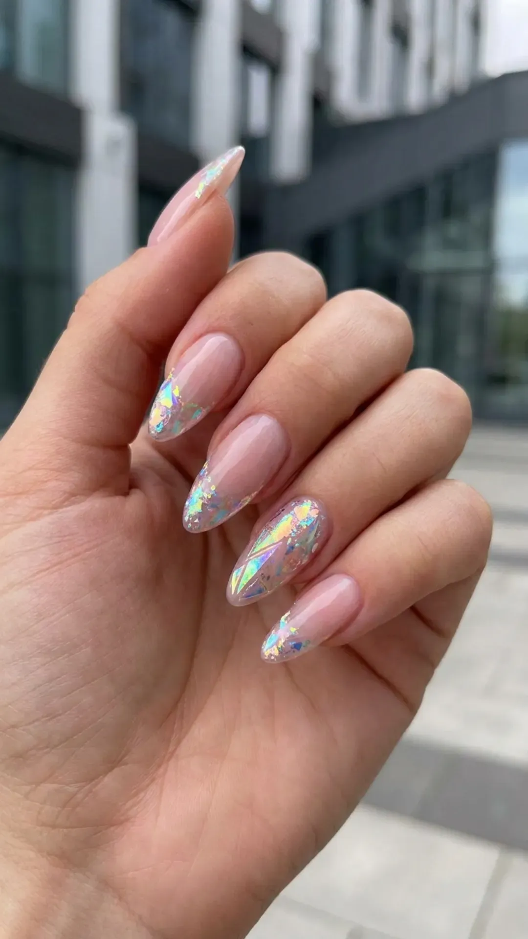 Sheer nude pink nails with striking holographic accents creating a futuristic rainbow effect, blending subtlety with a pop of iridescence.