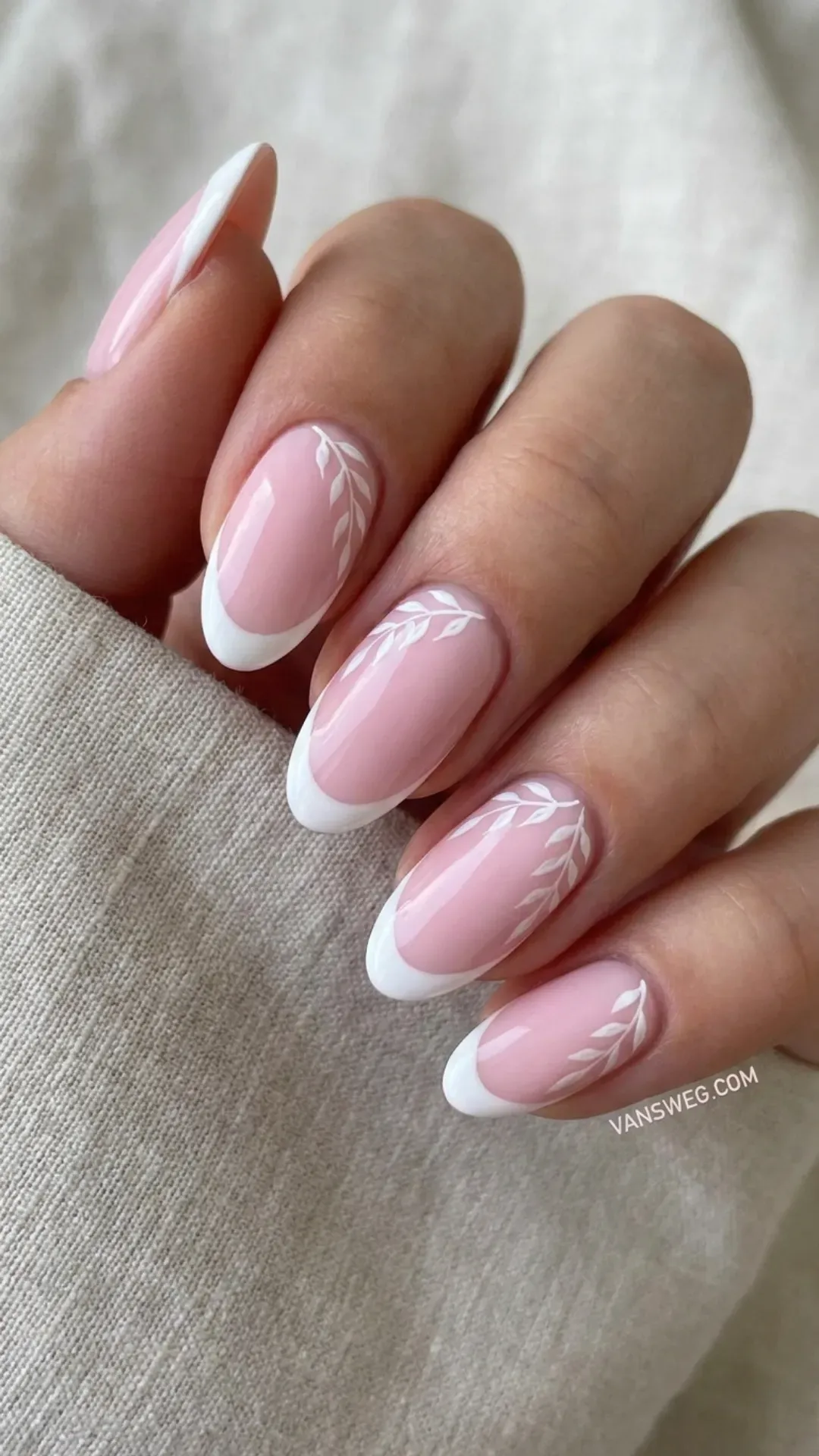 Modern French manicure on oval nails with a soft baby pink base, sharp white tips, and white leaf designs by VANSWEG.COM.