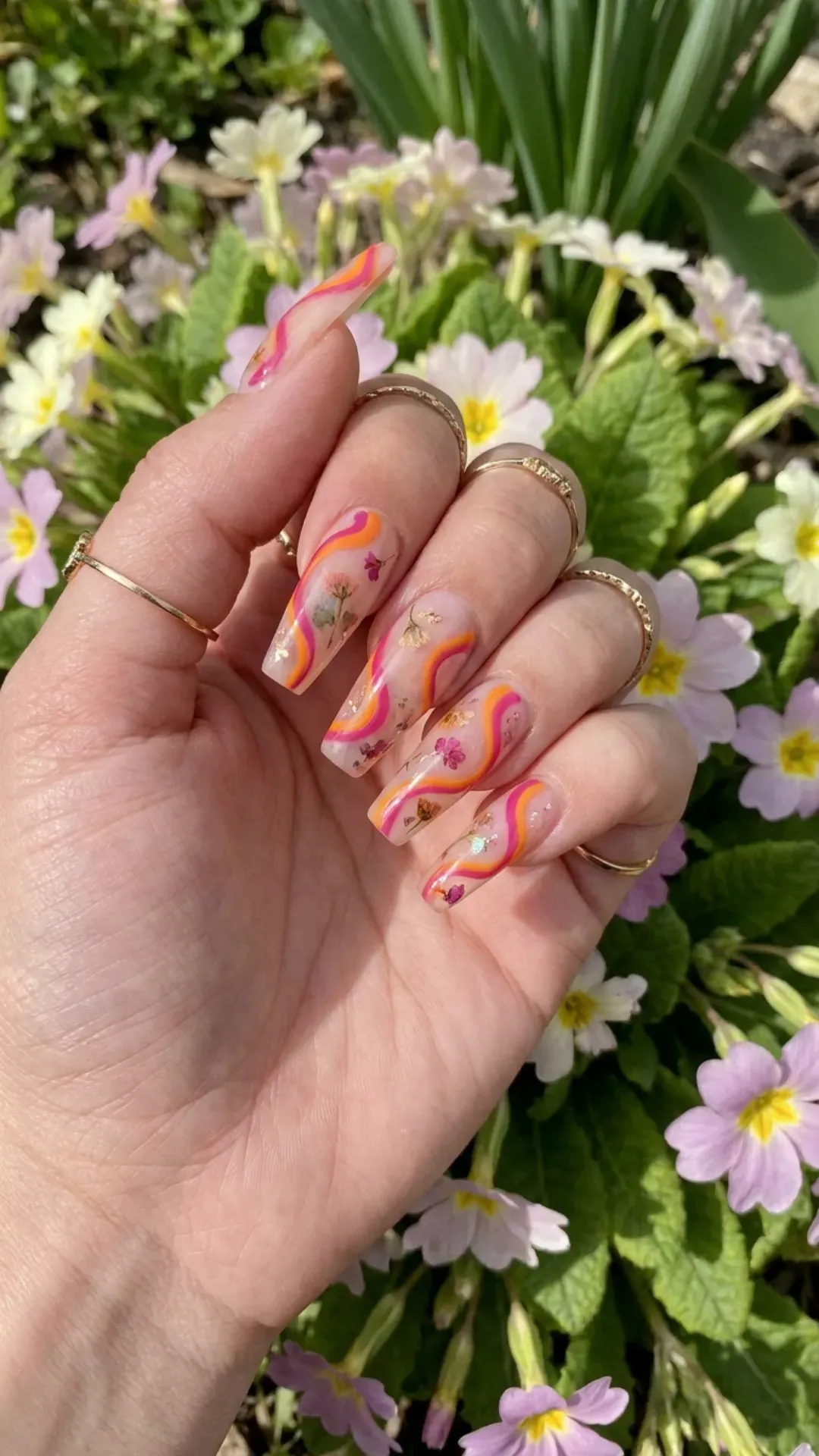 Vibrant coffin nails featuring a whimsical orange and pink swirl pattern on a sheer base, creating a fun and lively nail art look that captures the joyful essence of spring