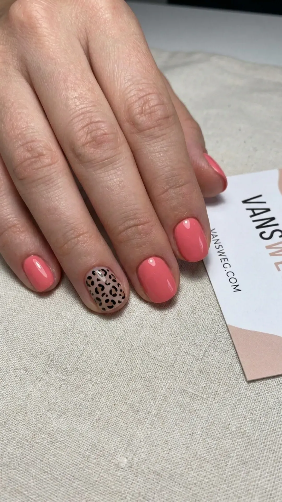 Short rounded coral pink manicured nails featuring a trendy black leopard animal print accent nail by VANSWEG.COM.