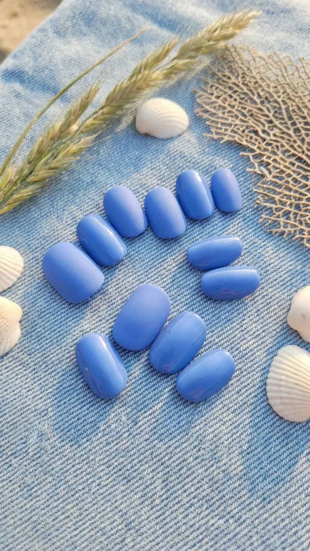 Medium round nails in soft cornflower blue with matte-to-glossy finish, styled on denim fabric, coastal summer vibes 2026