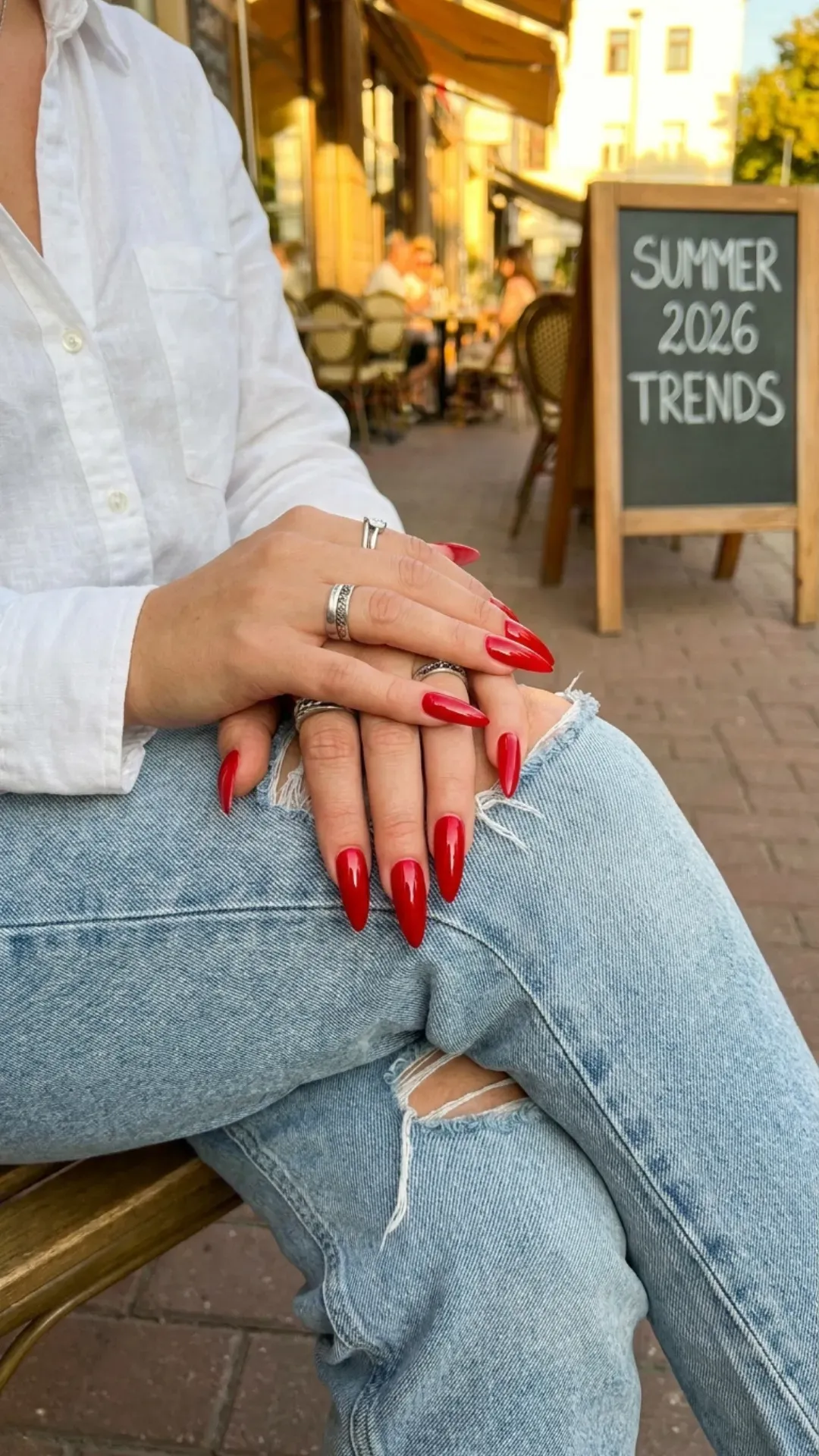 Bold red stiletto nails paired with jeans, highlighting a classic and daring color choice for summer 2026 trends.