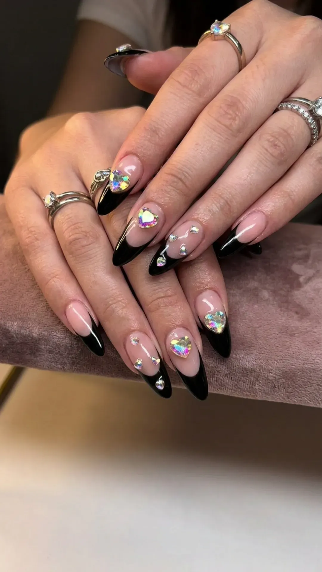 Black French tips adorned with oversized rhinestone hearts, creating a glamorous and bold statement manicure.