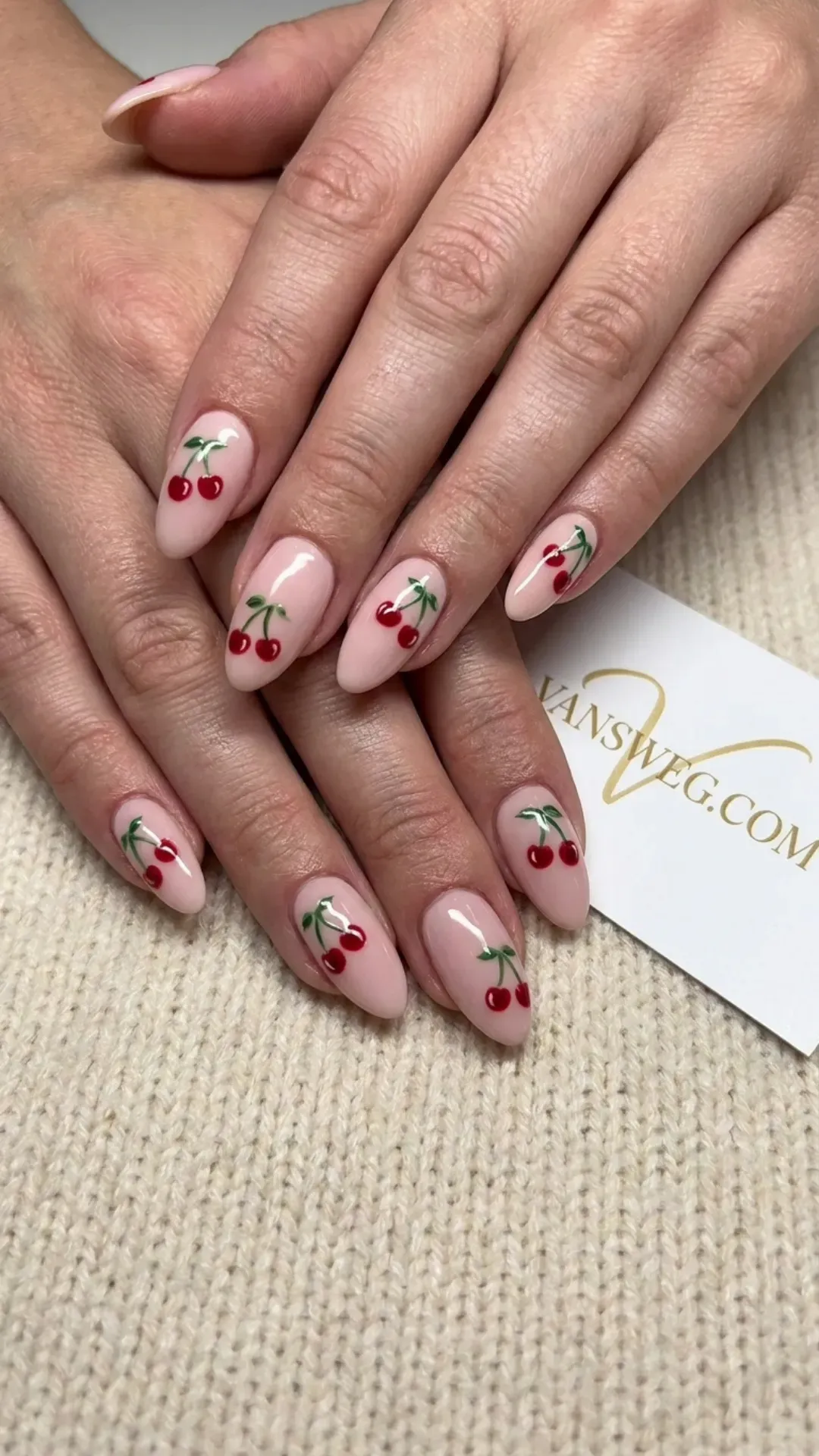 Medium almond-shaped light blush pink nails adorned with detailed hand-painted red cherry art by VANSWEG.COM.