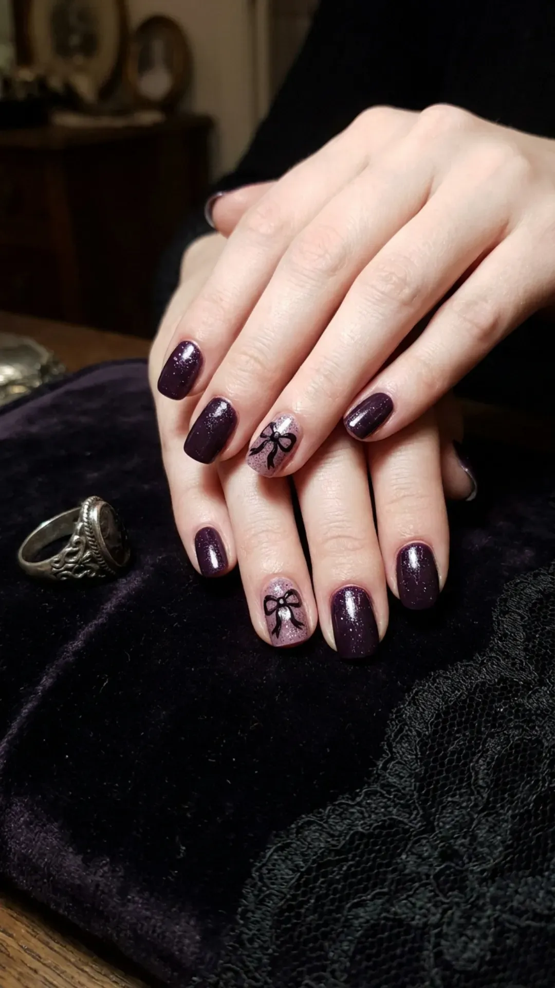 Dark purple nails with subtle sparkle and dainty bow designs, offering a gothic coquette aesthetic.