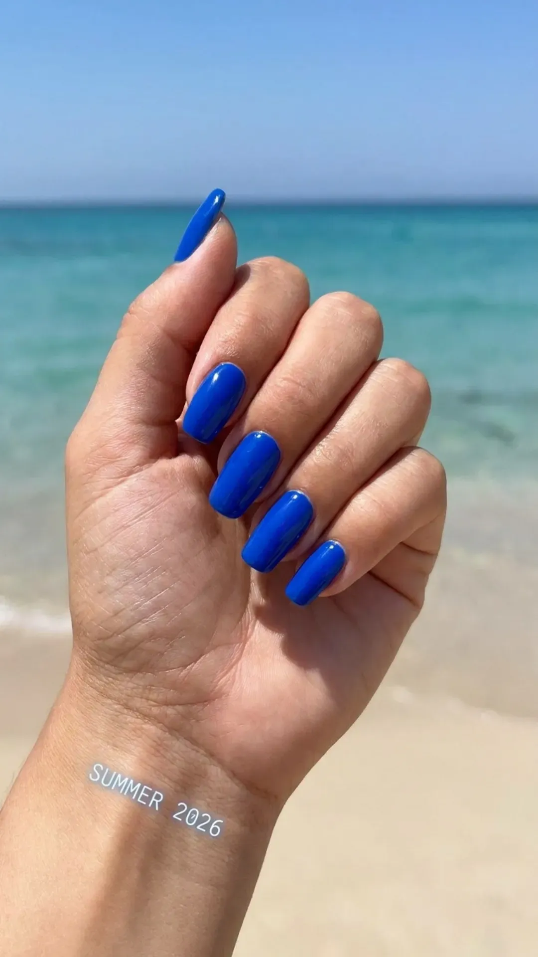Hand with electric blue nail polish, featuring a bold and striking color perfect for standing out this summer 2026.