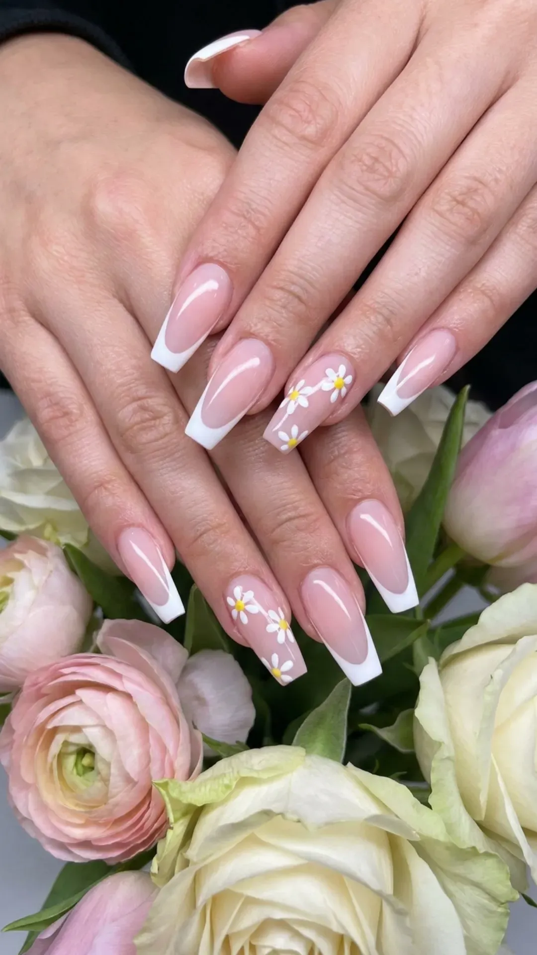 Long, coffin-shaped nails with a pink base and classic white French tips, enhanced with white daisy designs, providing a chic and feminine nail style perfect for spring.
