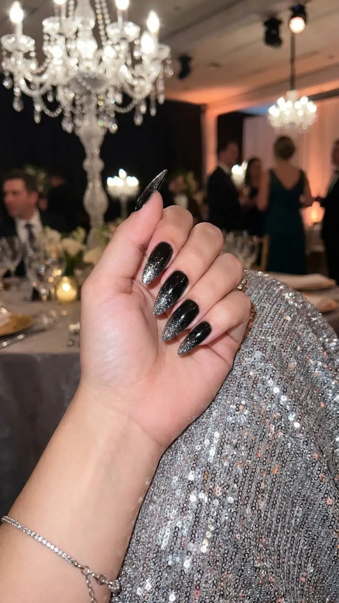 Luxurious long black nails dusted with fine silver glitter, matching a glamorous shimmering silver dress, perfect for a sophisticated gala event.