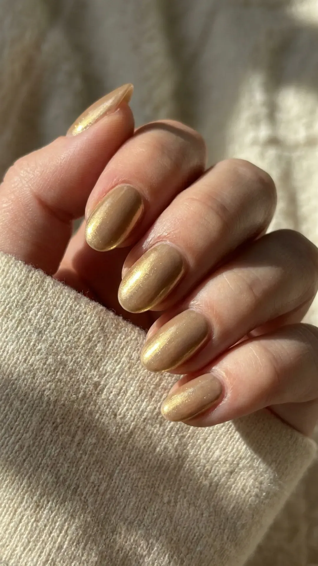 Medium oval nails with liquid gold chrome finish over nude beige base, warm molten glow in natural sunlight — 2026