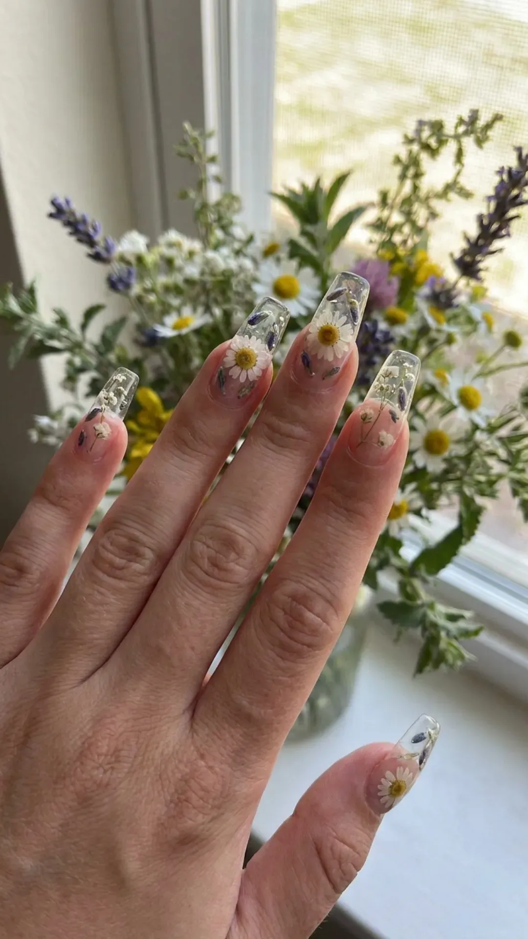Long clear gel extensions with real dried flowers — daisies, lavender, baby's breath — encapsulated in transparent gel — 2026 nails
