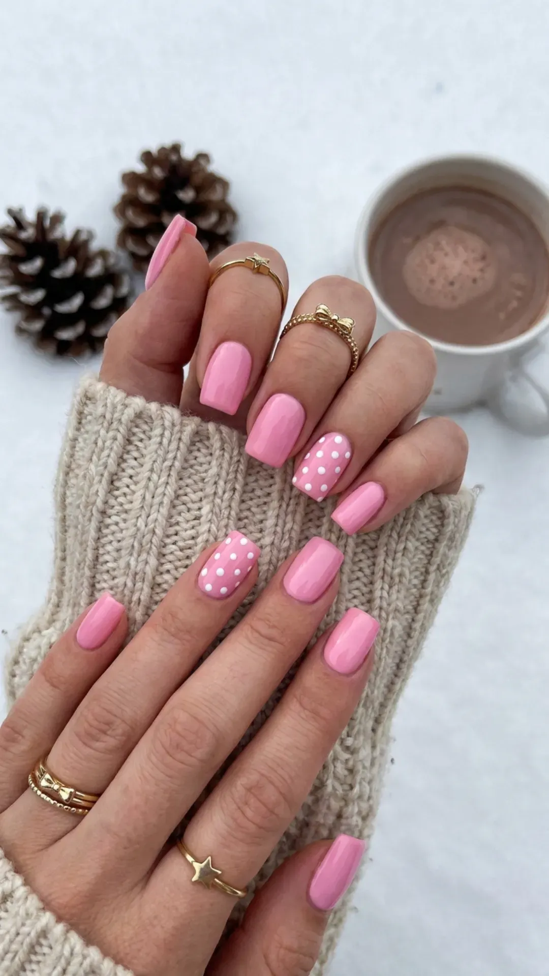 Chic and playful, these medium-length square nails feature a bubblegum pink base adorned with white polka dots on the ring fingers, paired with dainty golden rings for a whimsical winter look.